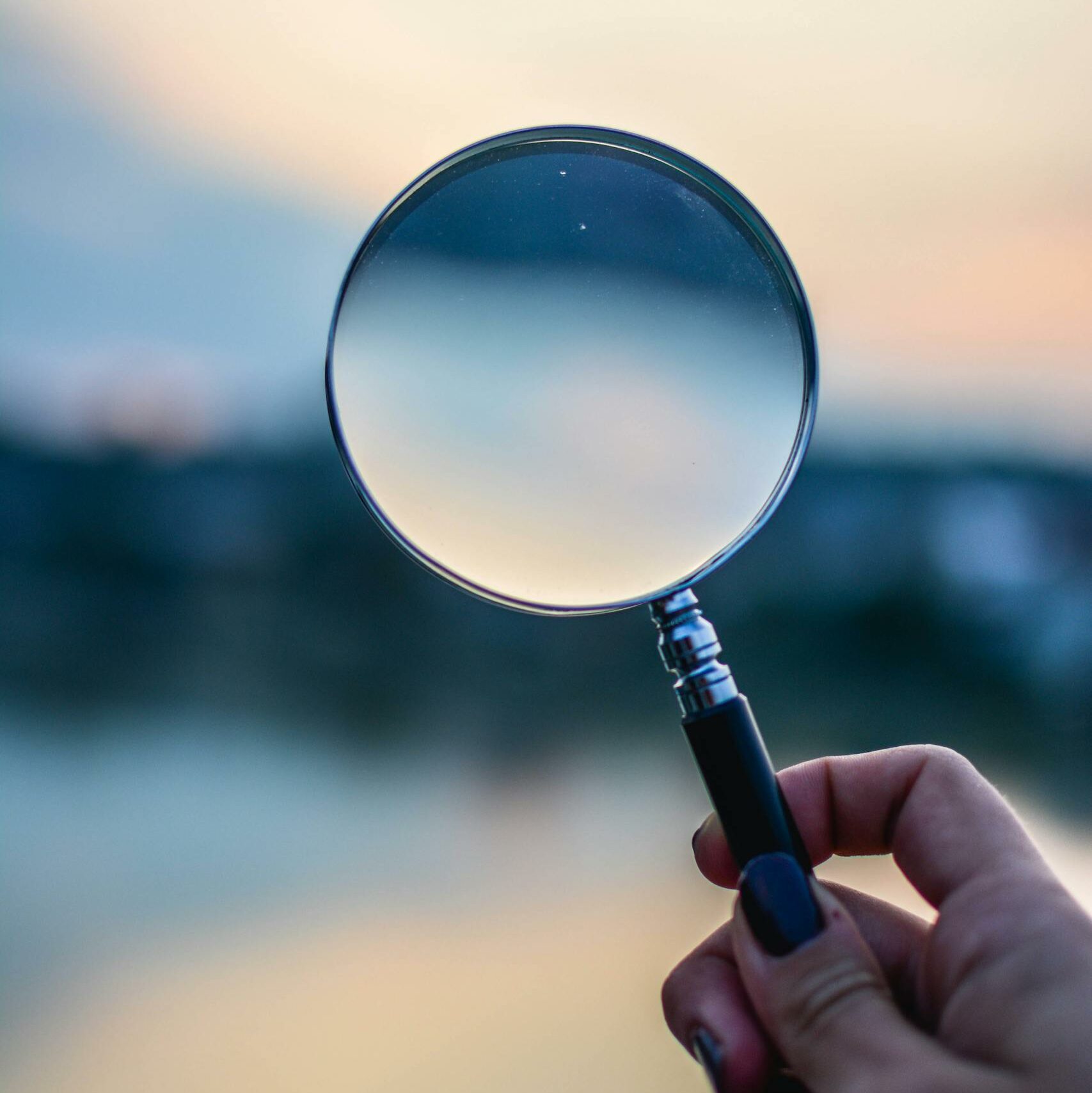 A magnifying glass held by a hand outdoors at sunset, focusing on exploration.